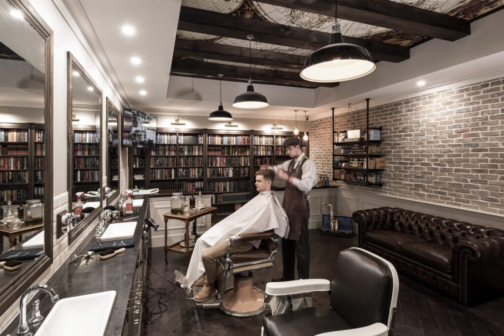 vintage style barbershop with brick walls, book shelves, & world map on the ceiling. Brown & white color scheme. 