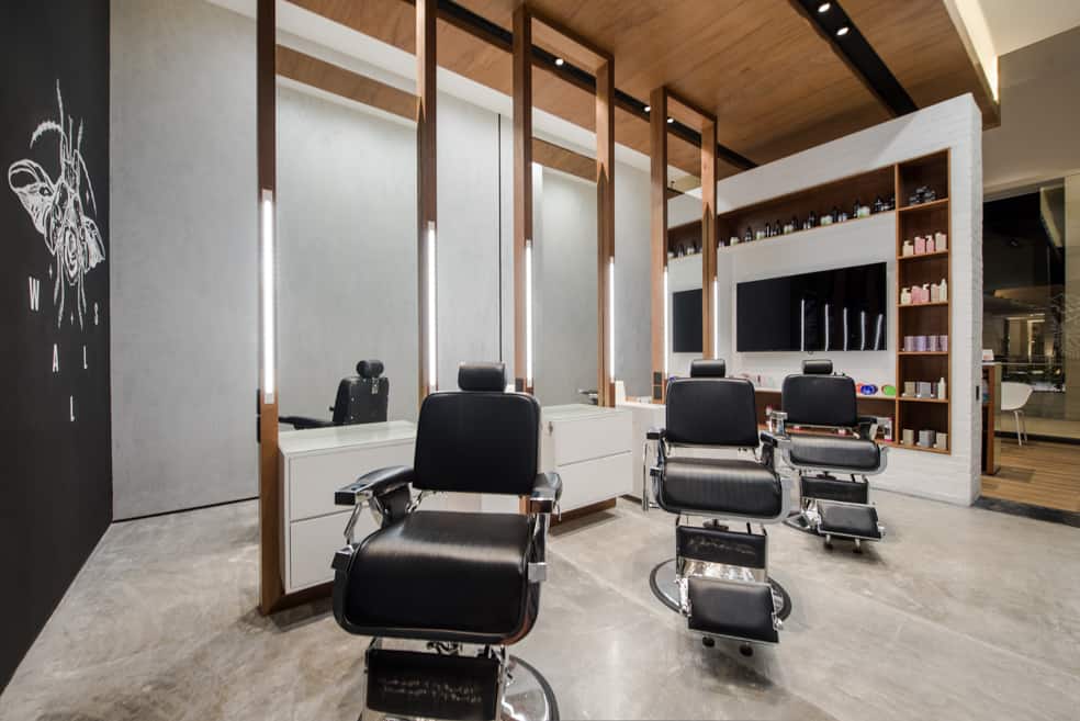 modern barbershop with wood syle walls & floor - black wall with logo painted on it & client chairs in the center of the room separate by floor-to-ceiling sized mirrors